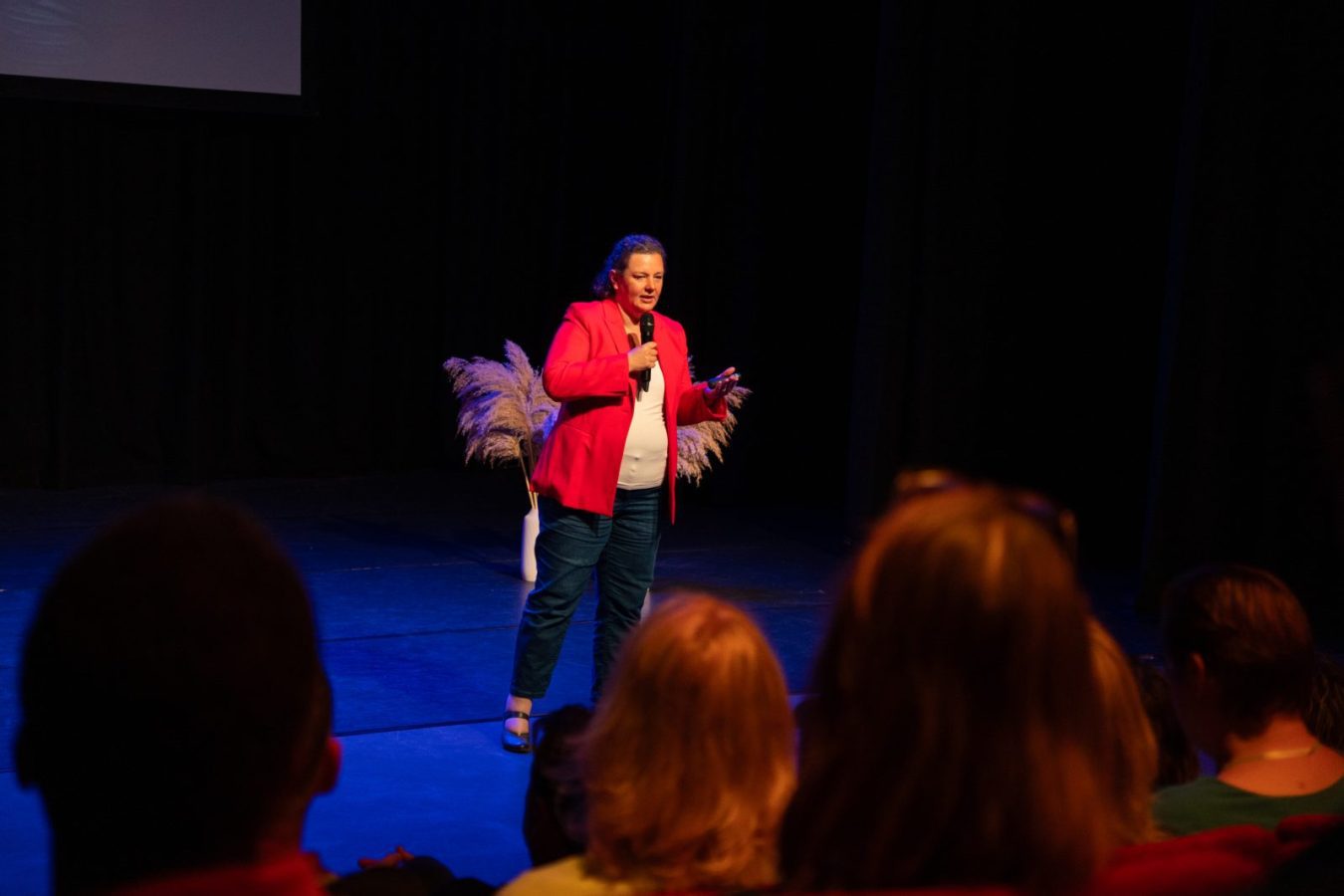 Nicole Schlösser op een podium voor een zaal met mensen, met achter haar een presentatie op een groot scherm.