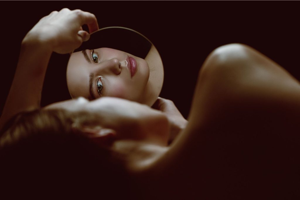 Vrouw kijkt in een klein rond spiegeltje – symbool voor hoe je zelfbeeld vaak vervormd is tijdens innerlijke strijd en spiritueel ontwaken.