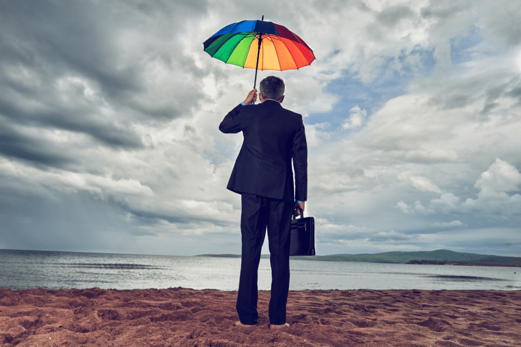 Man in pak op blote voeten op het strand met regenboogparaplu - symbool voor zelfbescherming uit eigenliefde